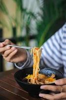 Essen Spaghetti Hand Geste im schwarz Schüssel mit Essstäbchen auf hölzern Tabelle foto