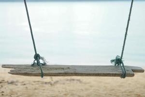 Holzschaukel der Nahaufnahme, die vom Baum mit altem Seil und verschwommenem Sand im Hintergrund hängt foto