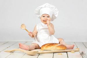 Kind kochen. wenig Mädchen im Koch Kleider mit ein groß Brötchen und Mehl. das Mädchen ist einer Jahr alt. ein Kind mit ein Ostern Brötchen. komisch Kind im ein kulinarisch Hut. foto