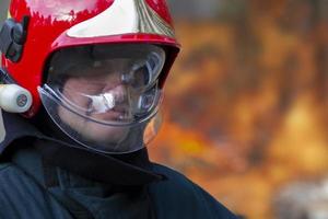 das Gesicht von ein Feuerwehrmann im ein Helm auf ein Hintergrund von Feuer. Putten aus ein Feuer. foto