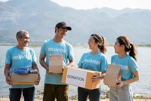 Mannschaft von Freiwillige lächelnd und halten Spenden Kisten, Spenden Tasche im draussen. Sozial Arbeiter Herstellung Anmerkungen Nächstenliebe foto