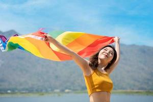 Lesben Frauen mit Fröhlich Stolz Regenbogen Flagge auf das Strand gegen das Himmel. jung Lesben Mädchen halten ein Regenbogen Flagge und umarmen glücklich. Unterstützer von das lgbt Gemeinschaft foto