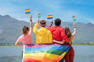 zurück Sicht. jung Vielfalt Menschen halten Fröhlich Stolz Regenbogen Flagge und bunt Turbine auf das Strand. Unterstützer von das lgbt Gemeinschaft foto