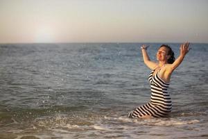 sich ausruhen beim das Erholungsort. ein Alten Frau auf Ferien durch das Meer Verbreitung ihr Waffen. foto