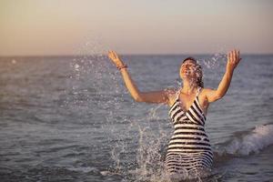 glücklich Frau im das Sonnenschein auf das Strand spritzt wasser.urlaub beim das Erholungsort. foto