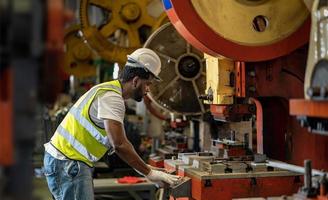 ein afroamerikanischer industriearbeiter verwendet eine hydraulische kraftpressmaschine, um metall- und stahlteile herzustellen, während er in der metallblechfabrik mit verzinktem dach für das konzept der sicherheitsindustrie arbeitet foto