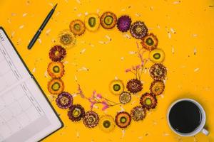 oben Aussicht Konzept von Pastell- Gelb Hintergrund bunt Blumen vereinbart worden im ein Kreis mit ein Notizbuch, Stift und Tasse von Kaffee platziert. Konzept, schreiben ein Notiz, Hintergrund, Natur schön Postkarte foto
