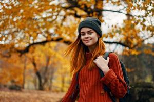 Porträt von ein Frau im ein Sweatshirt Hut mit ein Rucksack auf ihr zurück in der Nähe von das Bäume im Herbst im das Wald foto