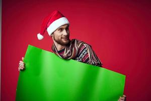 gut aussehend Mann im ein Weihnachten Hut mit Grün Attrappe, Lehrmodell, Simulation rot Hintergrund foto