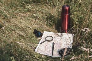 Karte, Lupe, Fernglas, Stift, Brille und ein Thermosflasche im das Gras. immer noch Leben von ein Reisender. foto