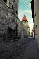 Stadt Straße von das alt Stadt im Tallinn mit ein uralt Mauer von Kalkstein und rot Fliese Dächer auf das Türme. das Straße ist eng. Dort ist ein Passage im das Mauer mit ein Treppe.. foto