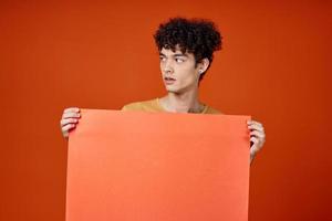 heiter Mann mit lockig Haar Poster im Hände Werbung Studio foto