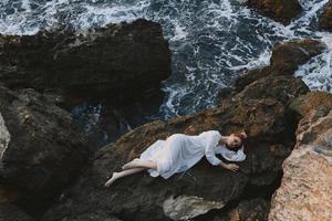 schön jung Frau Lügen auf ihr zurück auf ein felsig Strand Aussicht von über foto