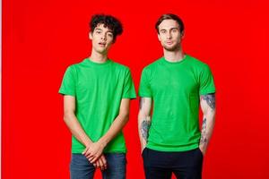 froh freunde im Grün T-Shirts sind Stehen Nächster zu rot Hintergrund foto