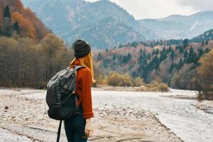 ein Reisender mit ein Rucksack im ein Sweatshirt und Jeans sind ruhen im das Berge im Natur in der Nähe von das Fluss im Herbst foto