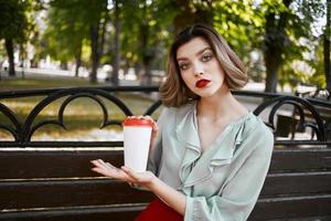 Frau Sitzung auf ein Park Bank mit ein heiß trinken draußen foto