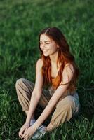 ein jung Frau im Sommer- Kleider Sitzung auf das Grün Gras tun Yoga und meditieren im Natur, ein Verbindung mit das Kosmos. das Konzept von Harmonie mit Körper und Natur, spirituell Wachstum foto