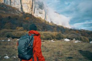 Frau im Jacken Kappen mit ein Rucksack auf ihr zurück Spaziergänge im das fallen im das Berge und im Natur foto