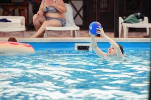 ein jung Mädchen hält ein Ball im ihr Hände während aktiv spielen im das Wasser von das Schwimmbad auf ein heiß Tag. aktiv Spiele im das Wasser im Sommer- foto