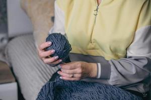 Nahansicht weiblich Hände halt ein Ball von Garn im ihr Hände und entwirren ein alt gestrickt Produkt foto