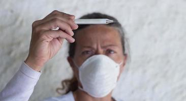 Erwachsene Frau mit Thermometer und Kinnriemen im Verhütung von Grippe Virus und Coronavirus foto