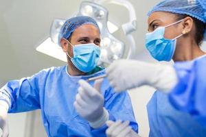 Low Angle Shot im Operationssaal, Assistent übergibt Instrumente an Chirurgen während der Operation. Chirurgen führen eine Operation durch. Professionelle Ärzte, die Operationen durchführen. foto