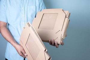 männlich Hand halten braun Karton Box auf Blau Hintergrund, Essen Lieferung und Verpackung Konzept foto