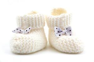 gestrickt Weiß Baby Booties mit Tupfen Bögen auf ein grau isoliert Hintergrund. Hintergrund. zum Text. Foto im hoch Qualität