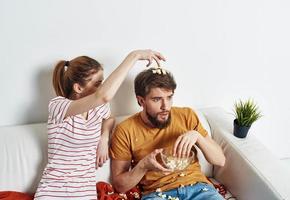 ein Frau im ein gestreift T-Shirt und ein Mann auf das Couch Aufpassen das Fernseher im ein hell Zimmer foto