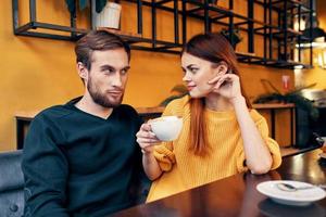 romantisch Frau Umarmungen ein jung Mann im ein Sweatshirt beim ein Tabelle im ein Cafe Innere ein Paar im Liebe foto