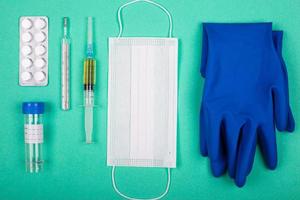 Pillen, Spritze, medizinische Handschuhe und Maske, Mittel zum Schutz vor Virusinfektionen auf blaugrünem Hintergrund
