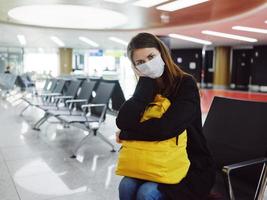 Frau mit müde Gesichts- Ausdruck medizinisch Maske warten Flughafen Passagier foto