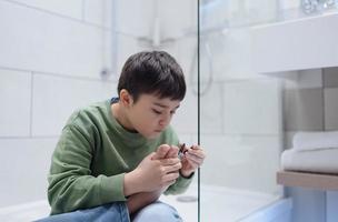 Porträt Kind Ausschnitt Nägel im das Badezimmer, Kind Junge Schneiden Zehe Nägel mit Nagel Haarschneidemaschine, Kinder Gesundheit und Hygiene Pflege, Pediküre Konzept foto