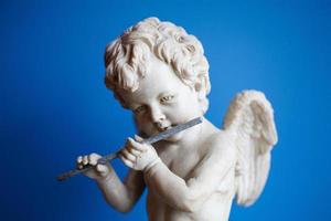 Statue von ein Engel spielen das Flöte auf ein Blau Hintergrund Porträt foto