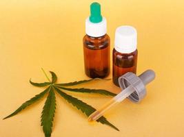 medizinischer Cannabisextrakt, der thc und cbd, medizinisches Hanföl und grünes Blatt auf gelbem Hintergrund enthält