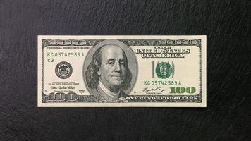 einer hundert Dollar Rechnung auf ein schwarz Teller Vorderseite Aussicht finanziell Konzept foto