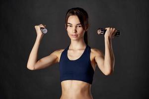sportlich Frau schlank Zahl Hanteln im das Hände von Fitness gepumpt oben Muskeln foto