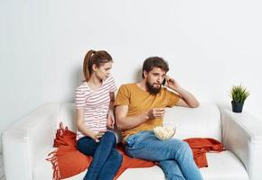 ein Frau im ein gestreift T-Shirt und ein Mann auf das Couch Aufpassen das Fernseher im ein hell Zimmer foto