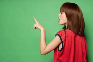 schön Frau im ein rot T-Shirt zeigt an ein Finger zu das Seite kostenlos Platz foto