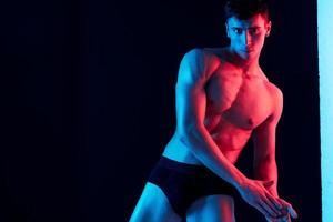 ein Mann mit ein sportlich Körperbau beugte sich vor zu das Seite und Neon- Licht schwarz Hintergrund Kopieren Raum foto