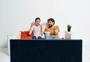 freunde Mann und Frau sitzen auf das Couch im Vorderseite von das Fernseher drinnen und ein Blume im ein Topf foto