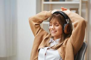 glücklich jung blond Dame Freiberufler im warm Sweatshirt im Kopfhörer Hör mal zu bewegt sich zu Liebling Lieder Tanzen Sitzung im Sessel beim Zuhause Innere. Musik- Zeit entspannend cool Wiedergabeliste Konzept. Kopieren Raum foto