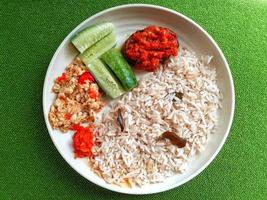Reis und Gurke und Sambal im ein runden Weiß Teller gegen ein Grün Hintergrund. foto