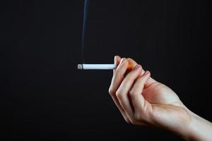 weibliche Hand, die eine rauchende Zigarette auf einem dunklen Hintergrund hält foto
