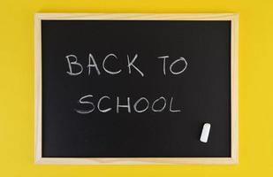 handgezeichneter Titel begrüßt zurück zur Schule auf schwarzer Tafel unter gelbem lebendigem Hintergrund.