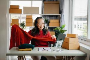Mode Blogger Konzept, Senior asiatisch Frauen Verkauf Kleider auf Video streaming.startup klein Geschäft klein, mit Smartphone oder Tablette nehmen erhalten und Überprüfung foto