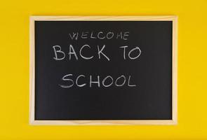 handgezeichneter Titel Willkommen zurück in der Schule auf schwarzer Tafel unter gelbem lebendigem Hintergrund.