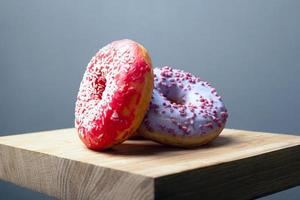 süße mehrfarbig sortierte Donuts mit Zuckerguss und Puder auf einem Holzbrett auf grauem Hintergrund