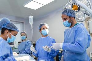 OP-Team, das Operationen in einem modernen Operationssaal durchführt, Ärzteteam, das sich während einer Operation auf einen Patienten konzentriert, Ärzteteam, das während einer Operation im Operationssaal zusammenarbeitet, foto