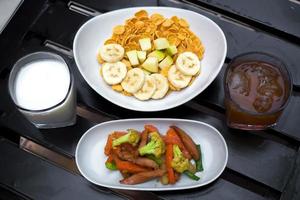 kontinental Frühstück Cornflakes mit Früchte, Milch und Tee und etwas von anbraten Gemüse auf schwarz Holz Tisch. oben Sicht. foto